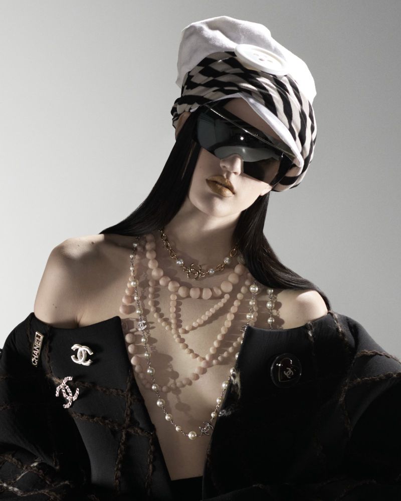 A fashion shot features a woman wearing a patterned turban, sunglasses, and multiple pearl necklaces, against a gradient grey background.