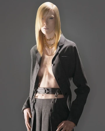Fashion portrait of a slender model with platinum blonde hair wearing a dark grey blazer and trousers with a belt and layered necklaces.
