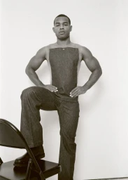 Saul Rodriguez posing with one foot on a chair wearing a sleeveless top and trousers for Fantastic Man Bodywear.