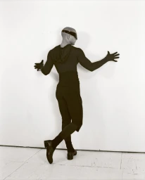 Model in black bodysuit and visor leaning against a white studio wall