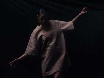 Woman in a textured patterned dress posing against a dark background for Crash Magazine.
