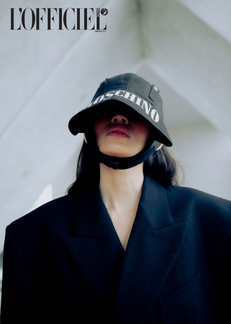 Fashion shot featuring a model in a black blazer and MOSCHINO bucket hat against a modern architectural backdrop.