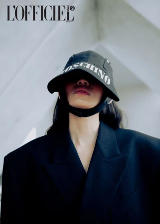 Fashion shot featuring a model in a black blazer and MOSCHINO bucket hat against a modern architectural backdrop.