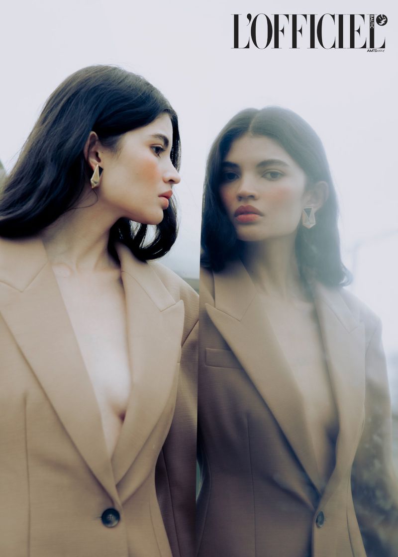 Brunette woman in beige blazer poses with a reflection in a minimalist outdoor portrait for a fashion editorial in L'Officiel magazine.