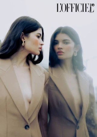 Brunette woman in beige blazer poses with a reflection in a minimalist outdoor portrait for a fashion editorial in L'Officiel magazine.