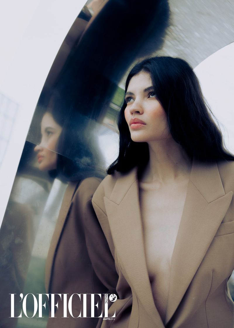 A woman in a blazer looks to her right, a glossy surface reflecting her profile, with the L'Officiel magazine logo visible at the bottom.