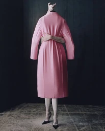 Model Saskia de Brauw wearing a pink coat with arms wrapped around the torso against a dark textured background