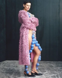 Model Saskia de Brauw in a textured pink coat with blue spheres against a dark paneled wall for Re-Edition Magazine.