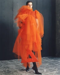 Model Saskia de Brauw in voluminous orange tulle dress standing against dark industrial backdrop for Re-Edition Magazine.