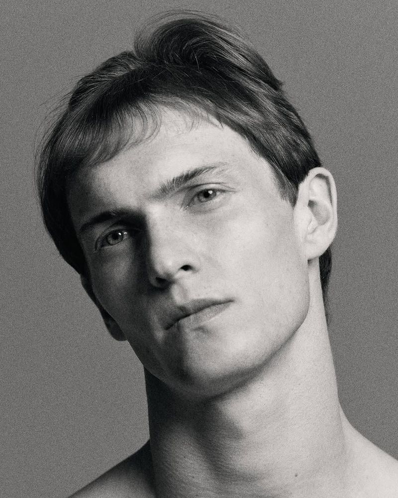 Monochromatic portrait of an adult male with short hair and light skin against a solid gray background in a studio setting.