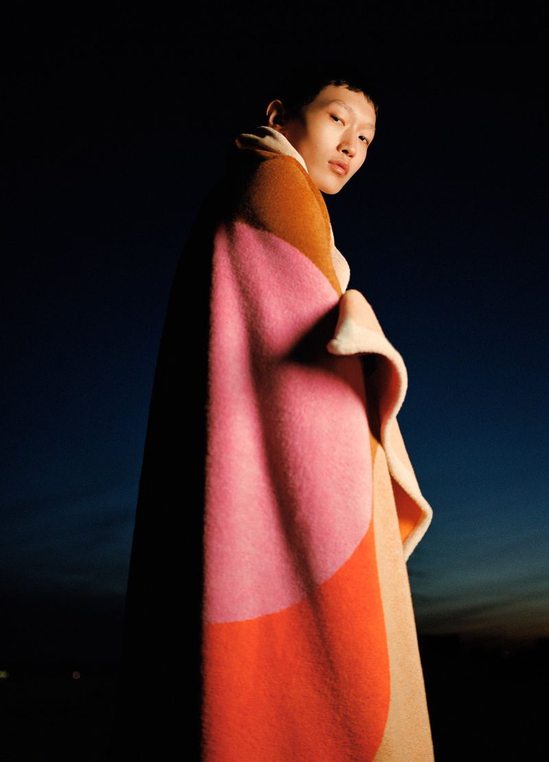 Asian adult posing in a colored blanket against a dark blue sky at twilight, fashionable and artistic image.