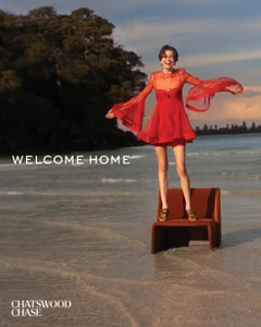 Smiling model in a red dress standing on a chair in the shallow water of a beach at sunset