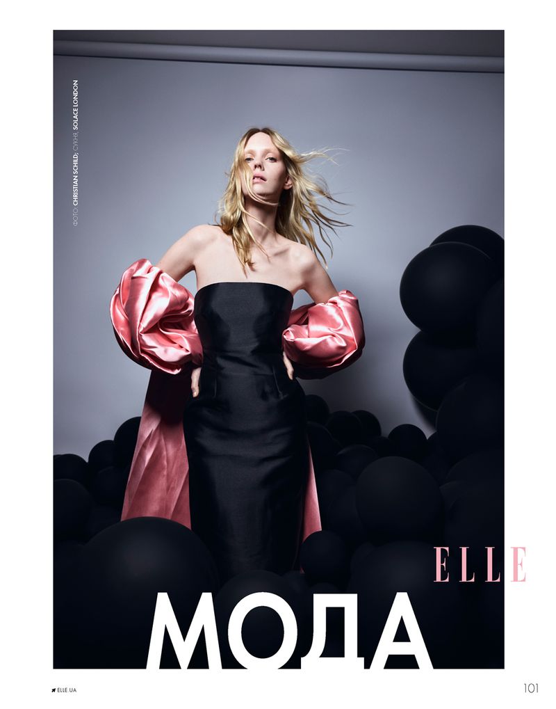 Fashion editorial cover featuring a blonde woman in a black dress with pink sleeves, posing against a backdrop of black balloons.
