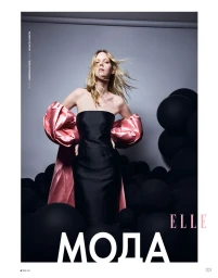 Model in strapless black dress with pink puffed sleeves standing amidst black spheres against a grey studio backdrop