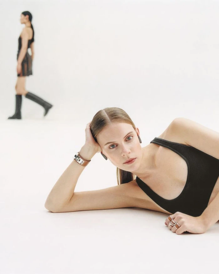 Model lying down in foreground wearing black tank top with another model walking in white studio background