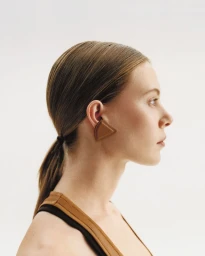 Profile portrait of a model with sleek brown hair wearing a triangular leather ear cuff against a plain white background