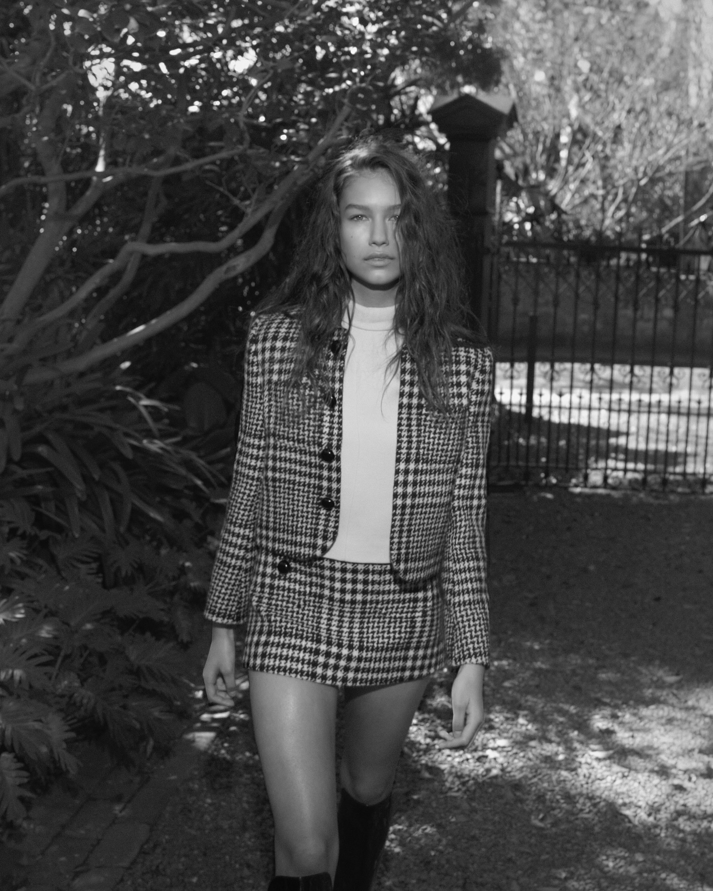 Model in houndstooth jacket and matching skirt standing outdoors near foliage for Side-note
