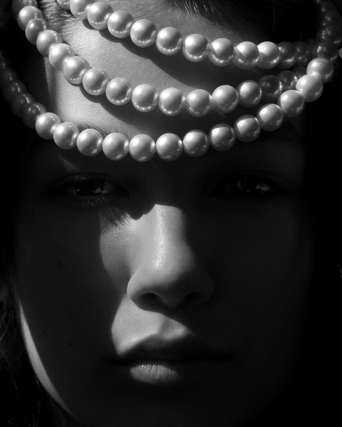 Close-up portrait of a young woman with a pearl necklace as a headpiece in black and white, showcasing beauty and fashion.