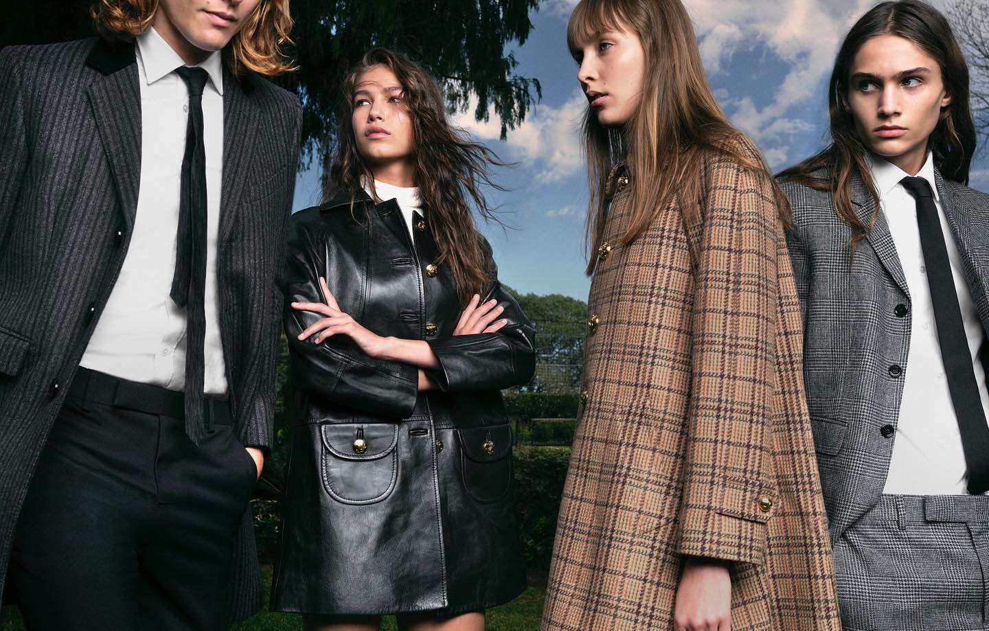 Four models showcase autumn fashion outdoors: two women in statement coats, and two men in classic suits, styled in an outdoor setting.