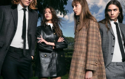 Four models standing outdoors against a leafy green backdrop and blue sky wearing tailored suits and coats.