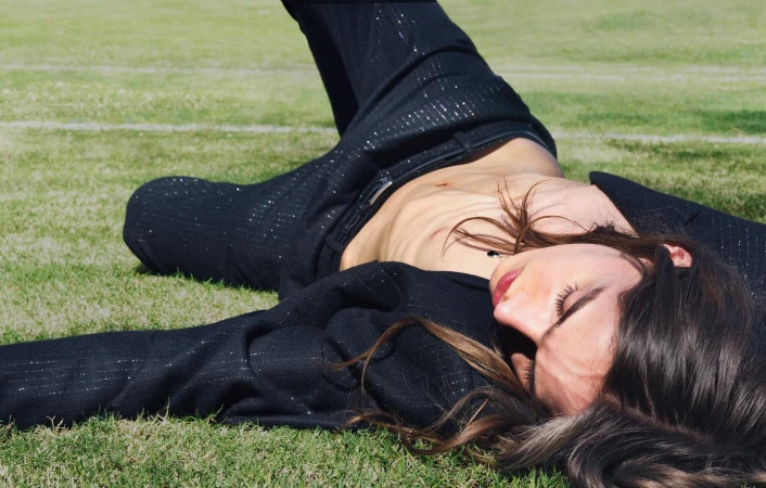 Model lying on green grass wearing a black suit jacket and trousers