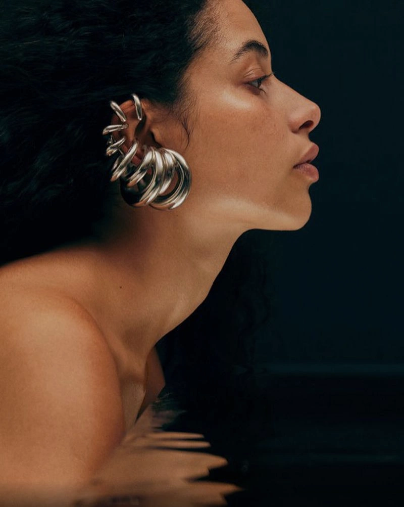 Close-up profile of a woman wearing chunky silver ear cuffs against a dark background