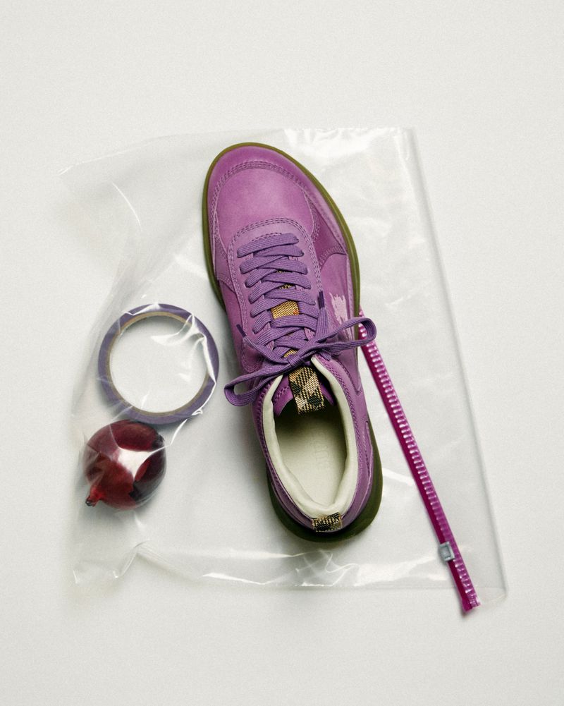 Still life of a purple sneaker, tape, and ornament in a clear plastic bag on a white surface in a studio setting. Flat lay style.