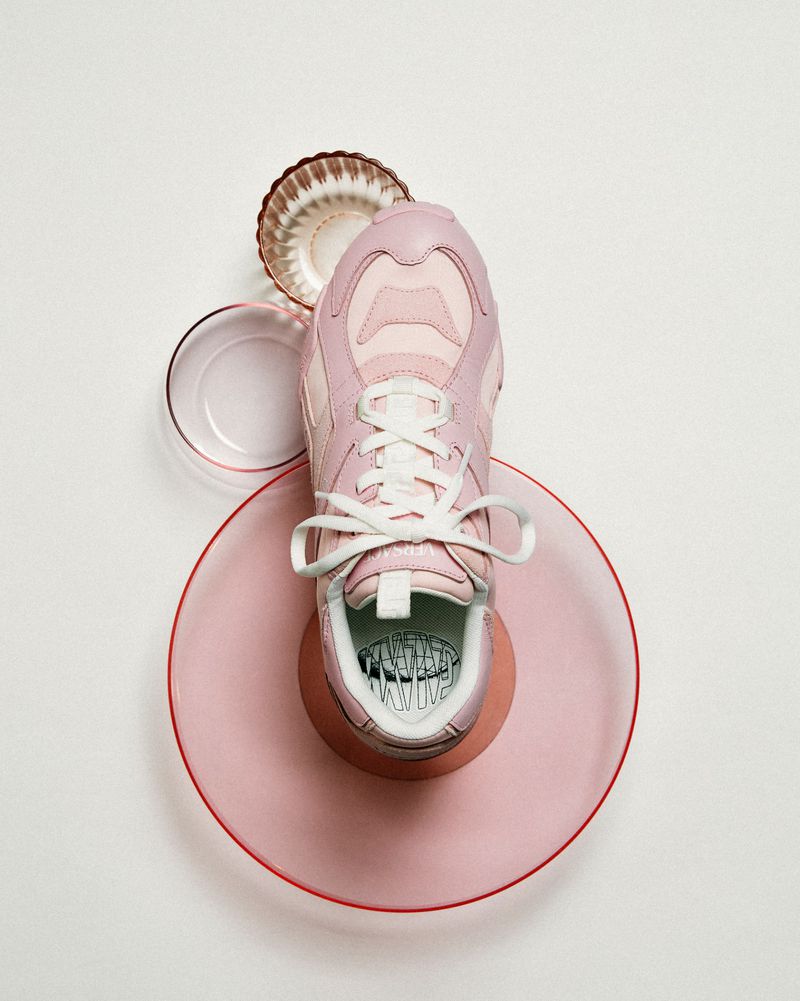 Pink sneaker presented on pink and white plates with a white background. Clean product photography with focus on color and texture.