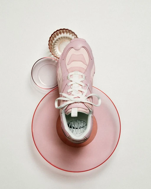 Pink sneaker presented on pink and white plates with a white background. Clean product photography with focus on color and texture.