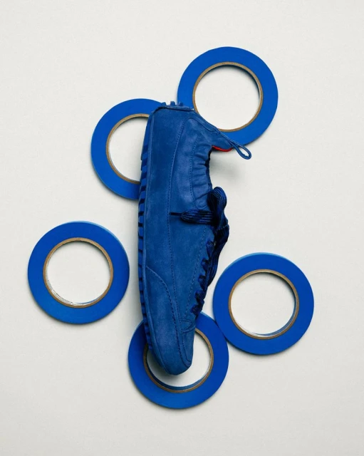 Eye-level still life of a blue suede shoe and five blue tape rolls arranged on a white background, creating a visually striking composition.