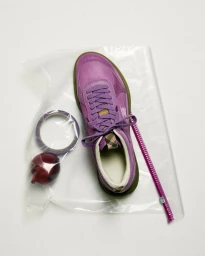 Top-down view of a purple sneaker, a roll of tape, and an onion inside a clear plastic bag against a white background.