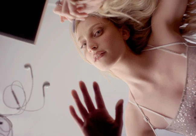 Low-angle portrait of a blond woman looking down with her hand out and headphones in the background, creating a dreamy, artistic effect.