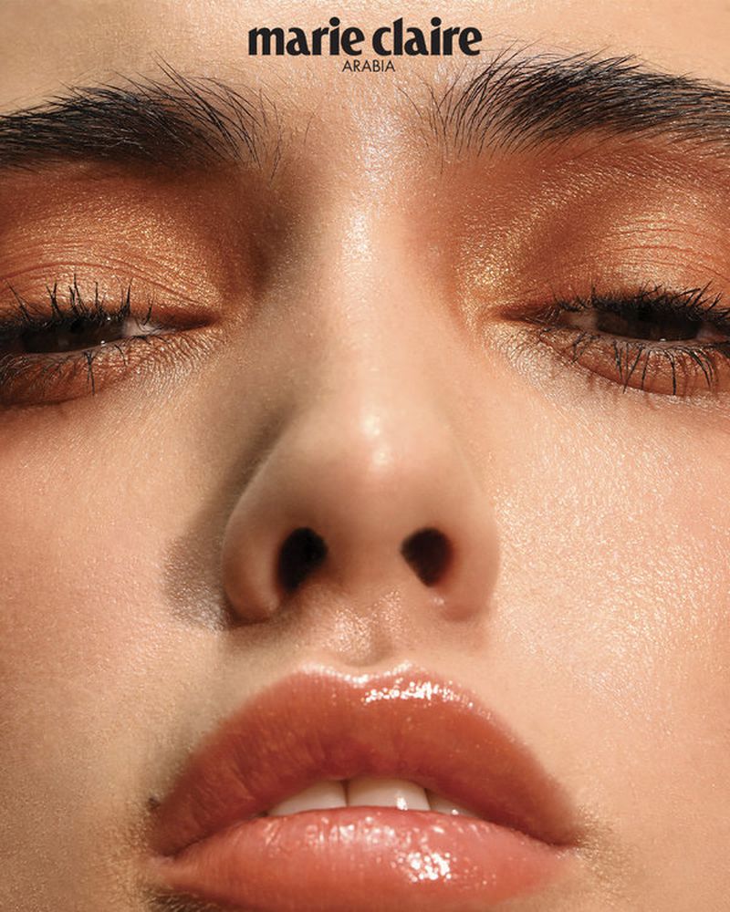 Close-up portrait of a woman's face, showcasing bronze-toned eyeshadow, glossy lips, and soft, even skin under diffused lighting.