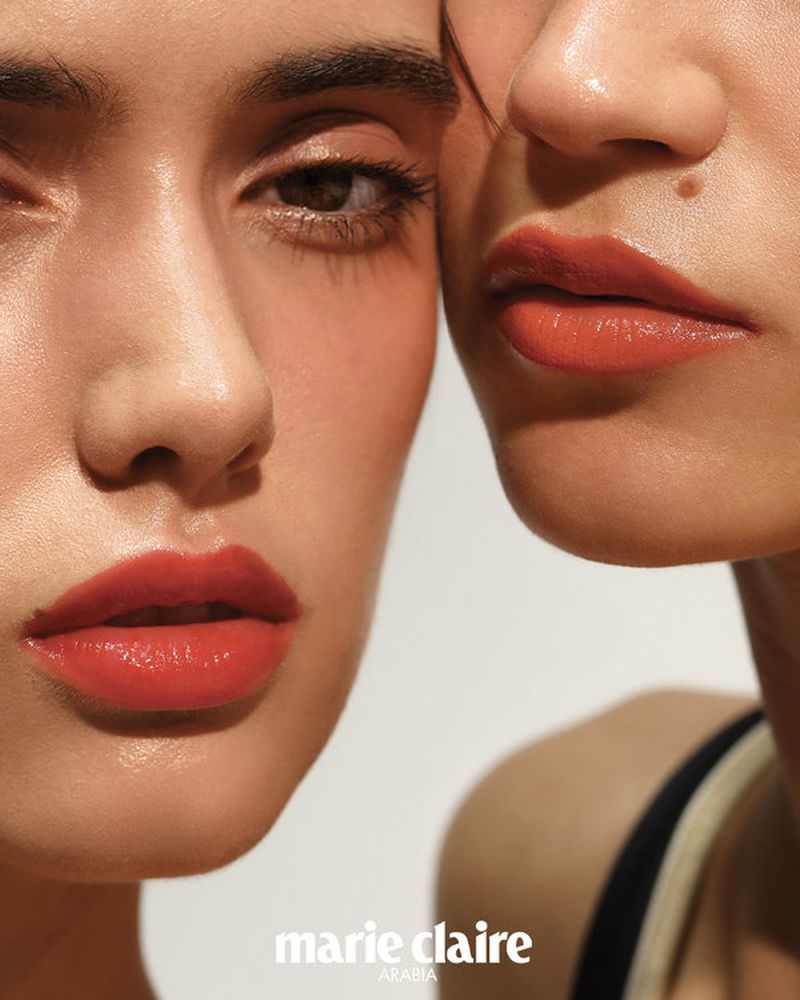 Close-up portrait of two young adult women with red lipstick, showcasing beauty and fashion in a bright indoor studio setting.