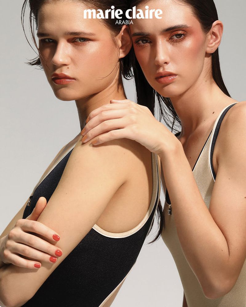 Two fashion models pose in a photo studio with neutral background. The models are wearing swimsuits and makeup for a beauty shot.
