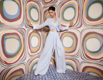 Model Aqua Parios wearing a light blue matching top and trousers posing against a colourful patterned wall