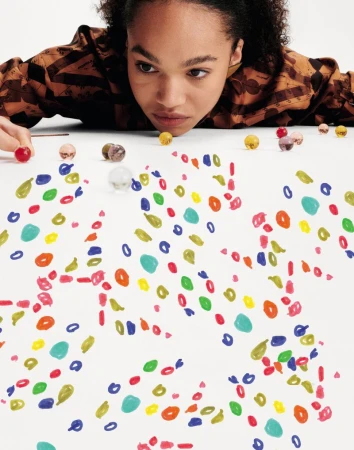 Woman gazes at colorful shapes and marbles scattered across a white surface in a close-up studio shot with shallow depth of field.