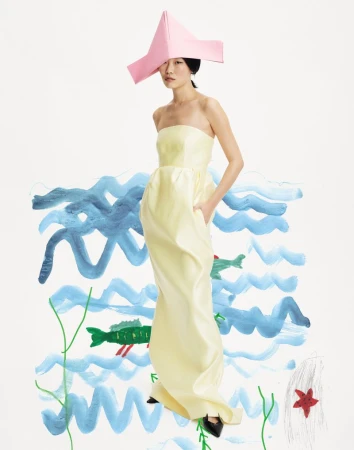 Elegant Asian woman poses in yellow gown and pink hat against a whimsical hand-drawn backdrop of ocean waves and sea creatures.