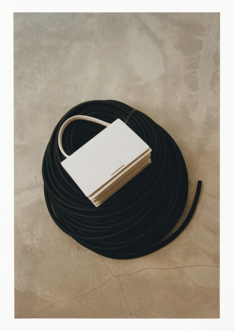 Elevated shot of a light-colored rectangular handbag with a handle resting on a coil of black tubing against a neutral background.