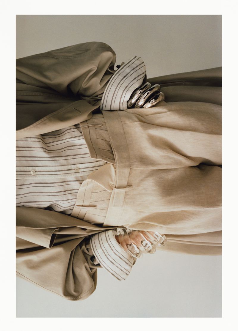 Beige trench coat and striped shirts arranged in a fashion still life against a neutral background in a studio setting.