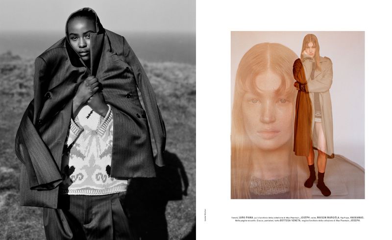 Fashion editorial shot of an adult female model wearing a gray oversized suit jacket and patterned sweater outdoors with ocean background.