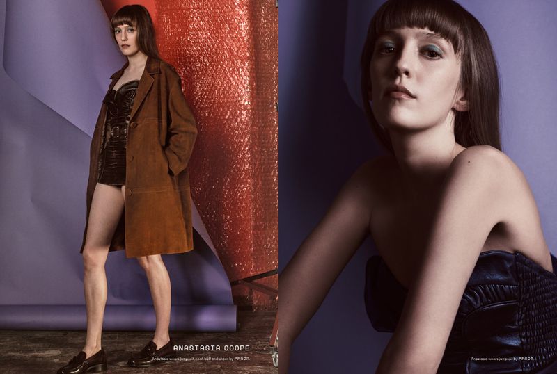 Fashion editorial shot of a young woman in brown coat and black loafers posing in a photo studio with a purple and red backdrop.
