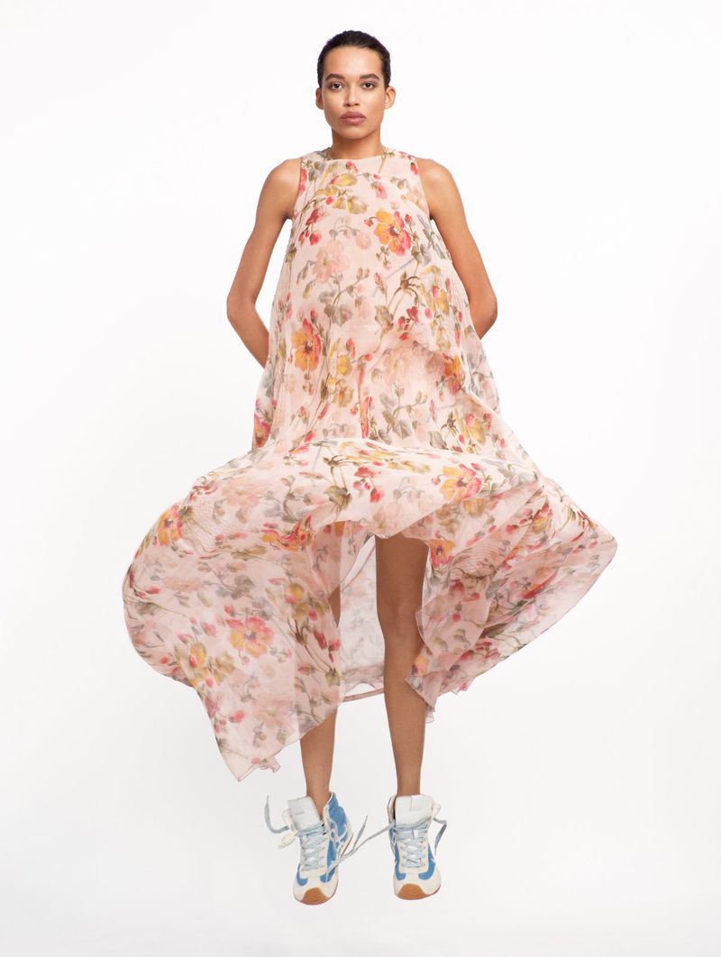 A woman is mid-jump, wearing a flowing floral dress and sneakers against a white background, creating a dynamic and fashionable image.