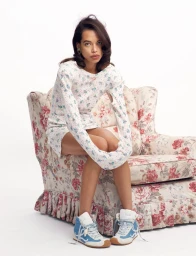 Model Lara Menezes seated in a floral armchair wearing a patterned long-sleeve top and blue high-top sneakers.