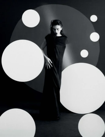 Elegant woman in a black dress poses in a studio surrounded by white circle props. Black and white studio fashion photography.