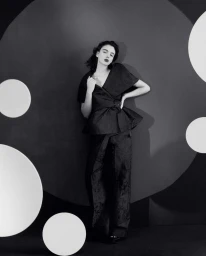Deva Cassel in a dark belted peplum top and trousers against a dark backdrop with large white circles for Re-Edition Magazine