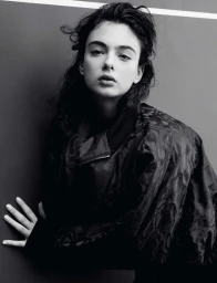 Model Deva Cassel posing in a dark textured jacket against a plain dark wall for Re-Edition Magazine.