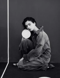 Deva Cassel squatting while holding a small white disc in a black and white editorial fashion photograph.