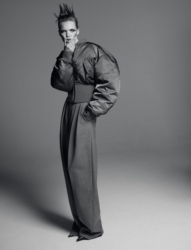 A monochrome fashion shot featuring a model in a puffy bomber jacket and wide-leg trousers against a grey backdrop, showcasing edgy style.
