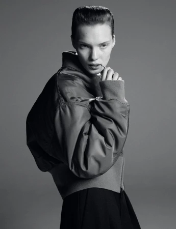 Monochromatic portrait of a young woman with a serious expression, wearing a bomber jacket against a grey backdrop.